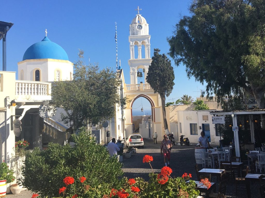 The main square of Megalochori village in Santorini with its blue dome and white bell tower