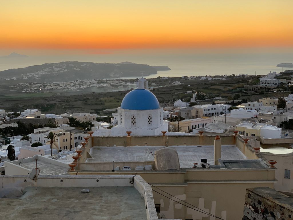 A blue-domed church in Pyrgos at sunset, looking across the caldera toward Thirassia