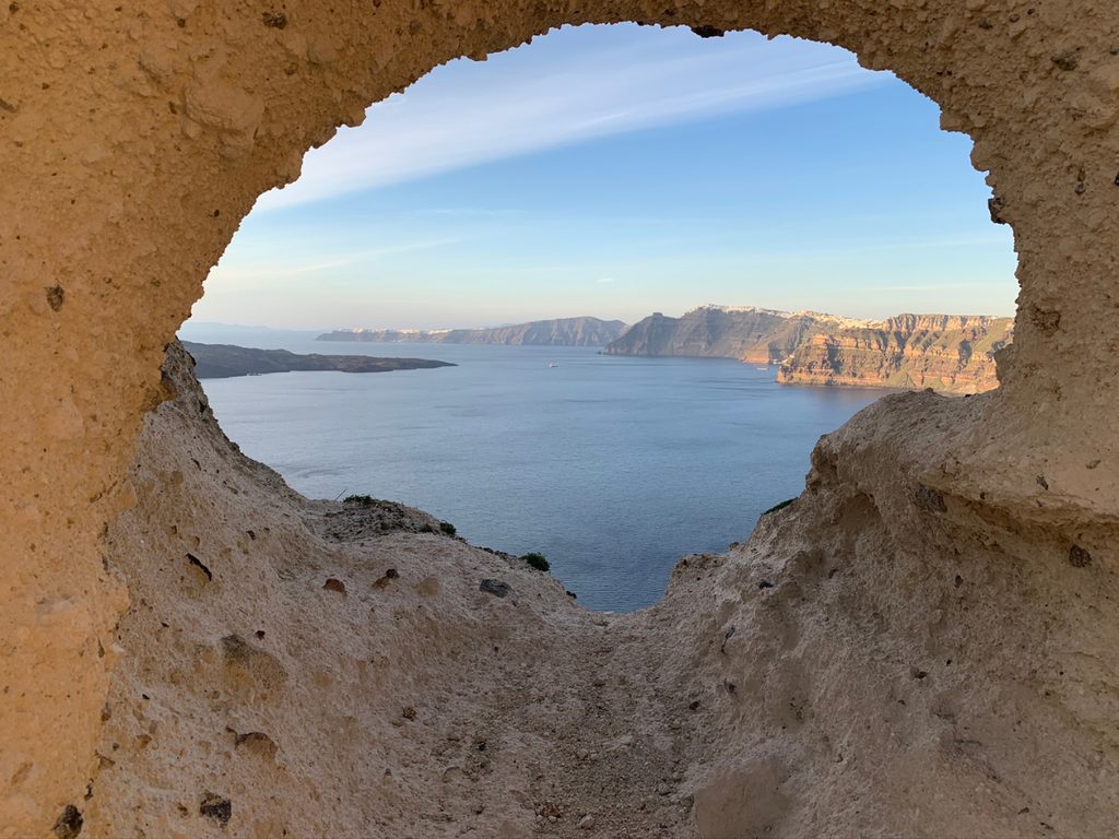 View of the Santorini caldera, Nea Kameni volcano and the Thirassia cliffs framed through a hole in volcanic rock